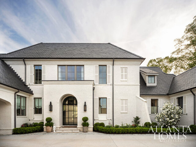 White brick house with dark roof, arched entryway, and manicured landscaping.