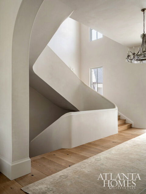 Interior with curved plaster staircase, wood floors, and crystal chandelier.