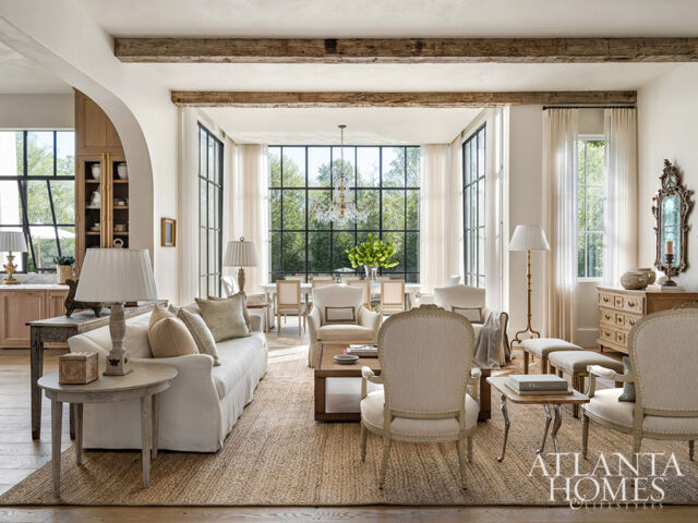 Living room with white sofa, armchairs, and dining area visible through large windows.