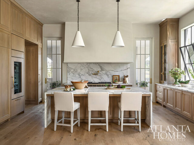 Kitchen with light wood cabinetry, marble island and backsplash, and white counter stools.