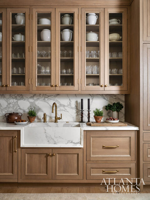 Wood cabinets with glass doors displaying white pottery and glassware, marble backsplash, and