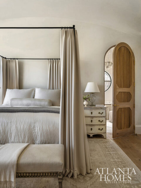 Bedroom with canopy bed, antique dresser, arched wooden door, and patterned rug.