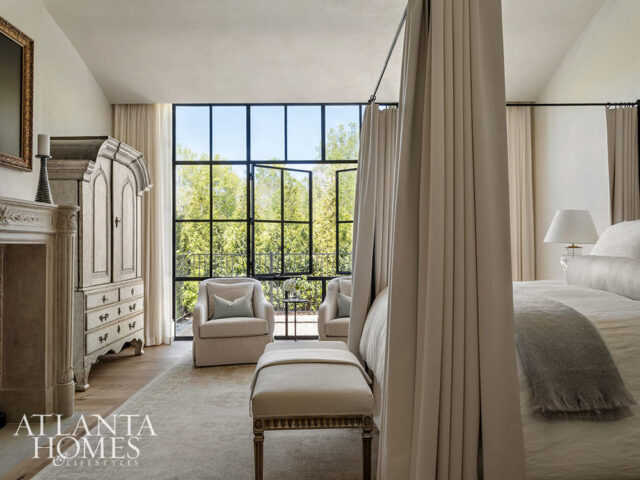 Bedroom with canopy bed, antique armoire, fireplace, and large window overlooking trees