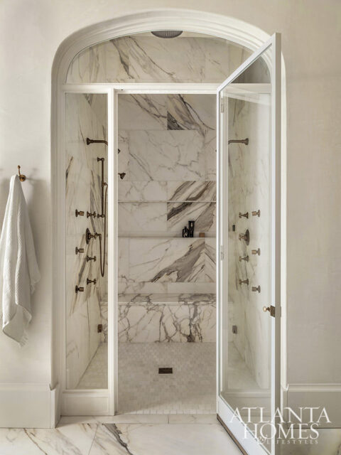 Arched entryway to marble shower with multiple shower heads and glass doors