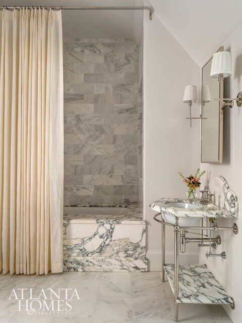 Marble bathroom with a freestanding sink, bathtub, and floor. Cream curtain hangs on the left.