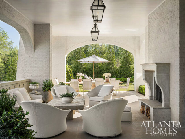 Covered patio with white furniture, stone fireplace, and arched openings to garden
