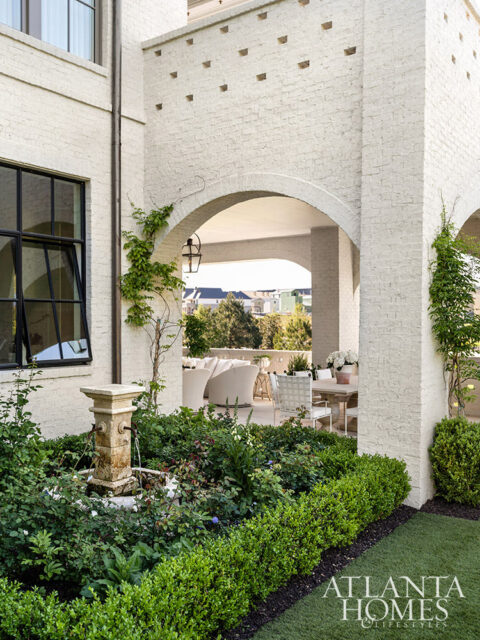 White brick exterior with arched entryway, fountain, and lush landscaping.