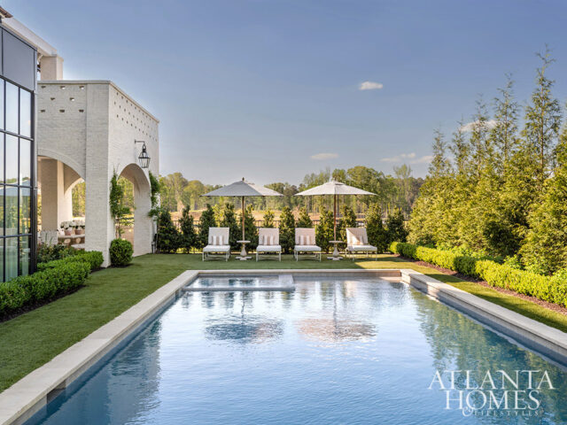 Rectangular pool with lounge chairs and umbrellas, adjacent to white brick archway and manicured