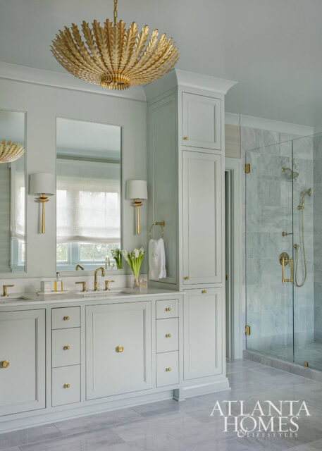 Light blue bathroom vanity with brass hardware, marble countertop, and gold chandelier.