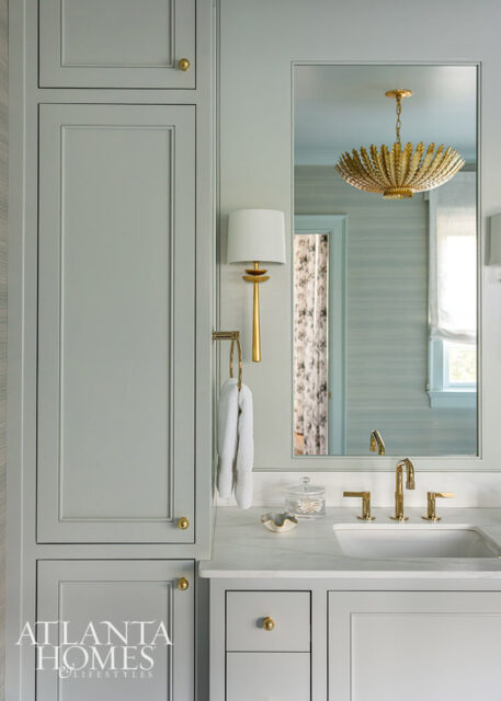 Light blue bathroom with marble countertop, gold fixtures, and a gold chandelier.