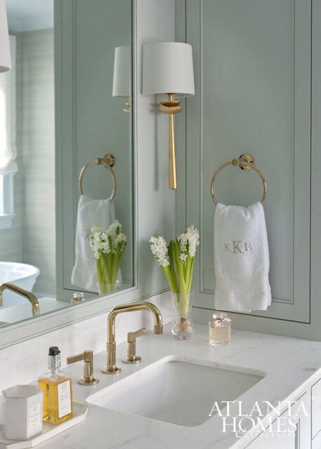 Pale green bathroom with marble vanity, gold faucet, and monogrammed towel