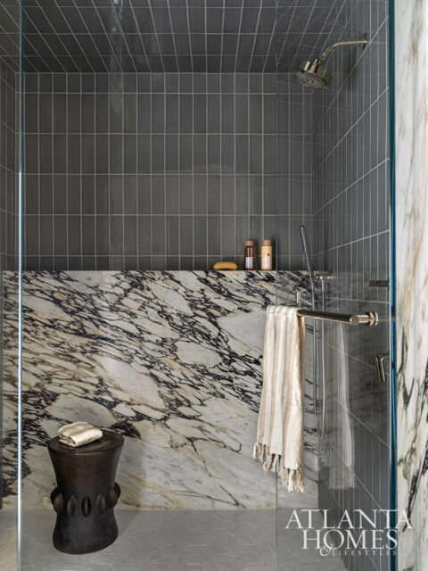 Shower with gray vertical tile walls, marble accent, and glass enclosure.