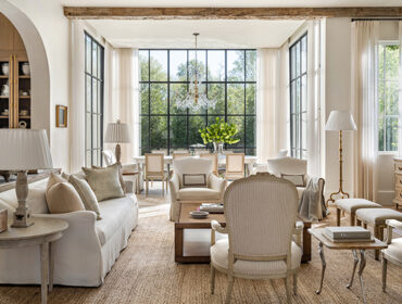 Living room with white sofa, armchairs, and dining area visible through large windows.