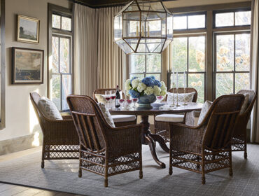 Dining room with wicker chairs, round table set for dinner, and large geometric chandelier.