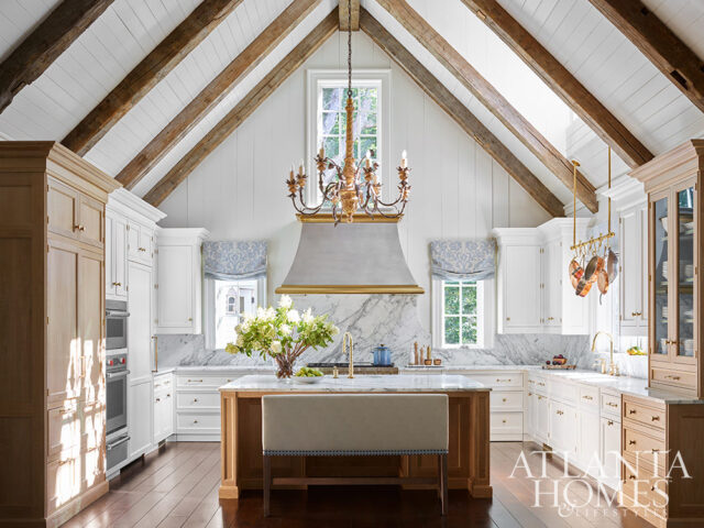White kitchen with marble counters, wood beams, and a large island with a bench seat.