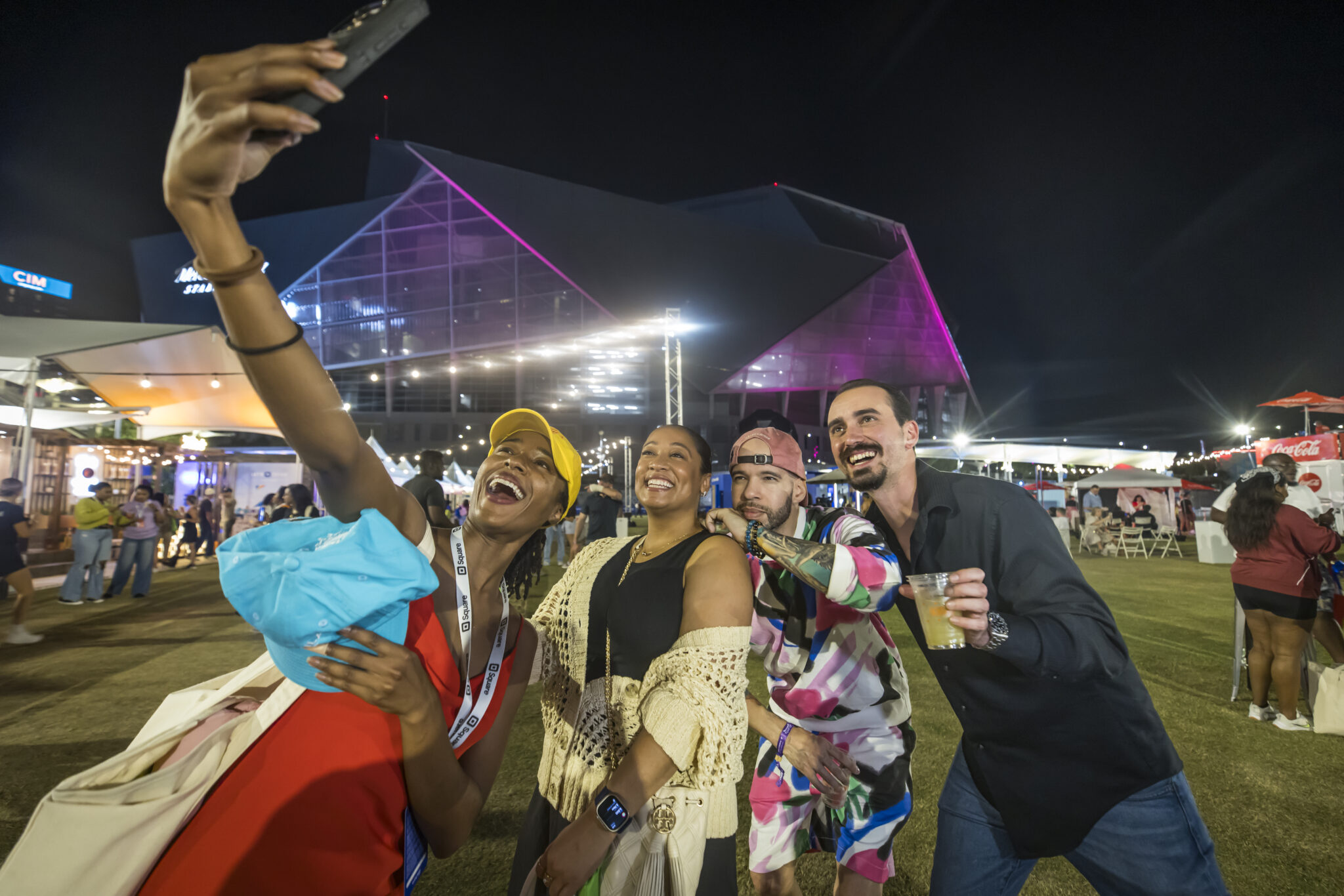 Four friends taking a selfie at night with a stadium in the background