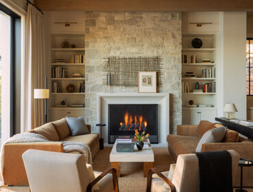 Living room with stone fireplace, built-in bookshelves, and tan sofas.