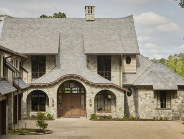 Stone house with arched entryway, multiple gables, and dormer windows.