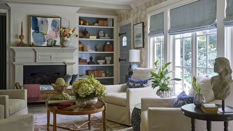 Living room with fireplace, built-in bookshelves, and large windows overlooking a garden.