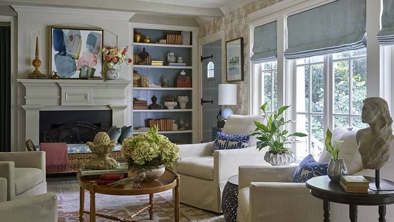 Living room with fireplace, built-in bookshelves, and large windows overlooking a garden.