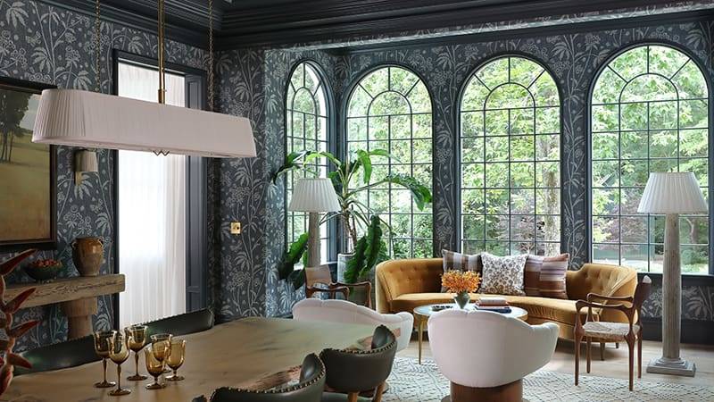 Dark wallpapered room with arched windows, mustard velvet sofa, and a wooden table.